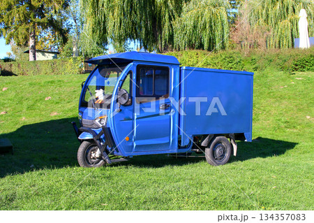 Blue utility vehicle parked on green grass near trees in a sunny outdoor setting 134357083