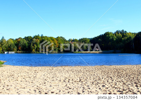 Scenic lakeside view with sandy beach and vibrant autumn foliage at midday 134357084