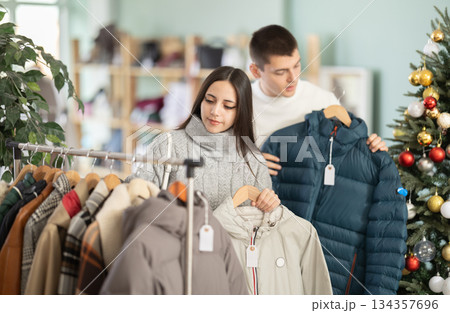 Young couple choosing coat or jacket in clothing store Young couple choosing coat or jacket in clothing store 134357696