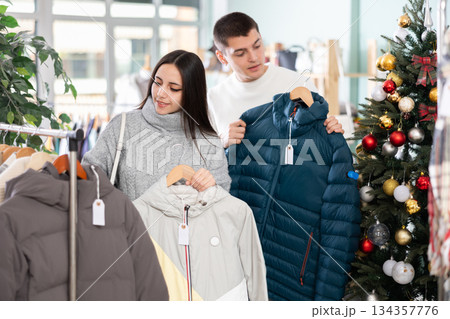 Young couple chooses down jackets in store Young couple chooses down jackets in store 134357776