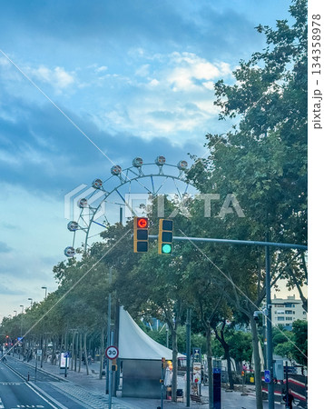 Cityscape with Ferris wheel, green traffic light, and blue evening sky. Urban travel mood with motion, funfair, and street life elements. High quality photo 134358978