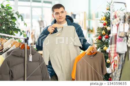 guy chooses cotton T shirts on the background of a Christmas tree guy chooses cotton T shirts on the background of a Christmas tree 134359635