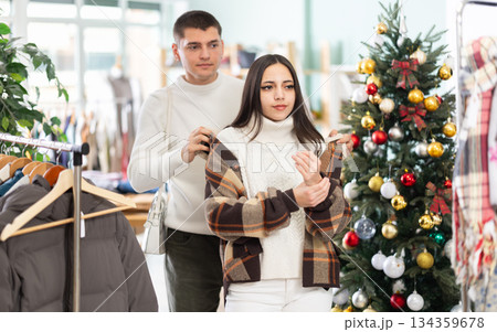 Couple standing in shop and choosing warm winter clothes in Christmas shop Couple standing in shop and choosing warm winter clothes in Christmas shop 134359678