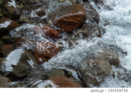Close up fresh waterfall stream rushing over wet brown river rocks texture in a natural setting. 134359758