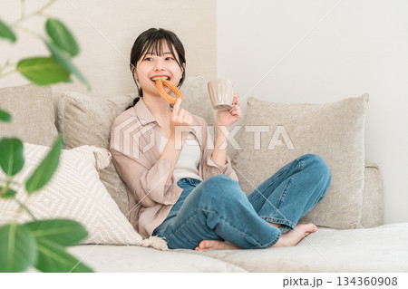リビングのソファーに座りドーナツを食べる若いアジア人女性 134360908