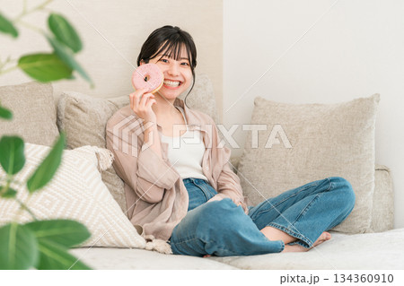 リビングのソファーに座りドーナツを食べる若いアジア人女性 134360910