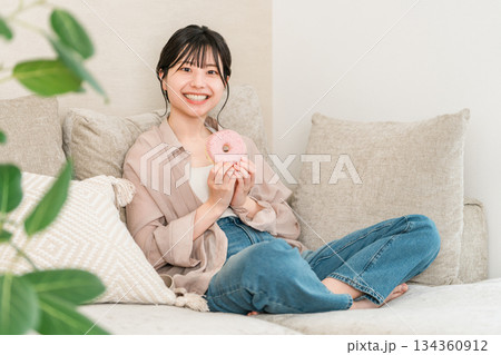 リビングのソファーに座りドーナツを食べる若いアジア人女性 134360912
