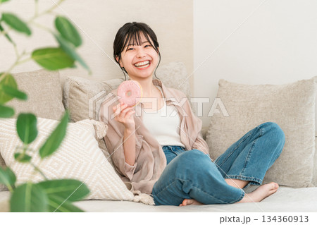 リビングのソファーに座りドーナツを食べる若いアジア人女性 134360913