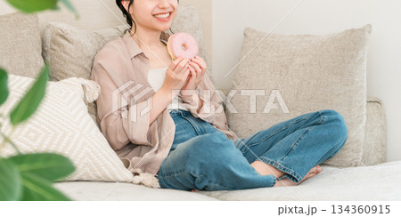 リビングのソファーに座りドーナツを食べる若いアジア人女性 134360915