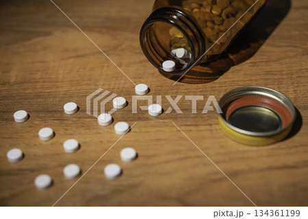 テーブルにこぼれた白い錠剤と茶色の遮光瓶 134361199