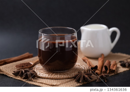 Hot chocolate in glass and star anise and cinnamon sticks on black background Hot chocolate in glass and star anise and cinnamon sticks on black background 134361636