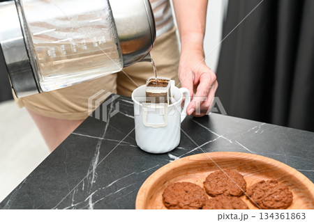 Hot water is poured over a drip coffee filter, creating a clean filtered brew known for smooth taste, lower acidity and health benefits during a calm home break. 134361863