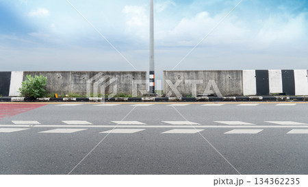 Horizontal or landscape view of side view asphalt road. with concrete roadside barriers and a steel lamppost in the center. under blue sky and white clouds. Horizontal or landscape view of side view asphalt road. with concrete roadside barriers and a steel lamppost in the center. under blue sky and white clouds. 134362235