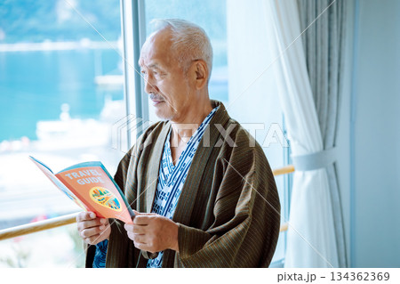 窓辺でガイドブックを読む年配男性 134362369