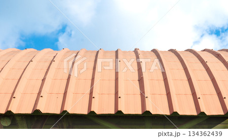 Roof of metal sheet orange color is faded and curved sheet. On steel structure. Background of blue sky and white clouds. Roof of metal sheet orange color is faded and curved sheet. On steel structure. Background of blue sky and white clouds. 134362439