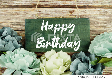 Happy Birthday text written on wooden plank with flower decoration on wooden background 134364706
