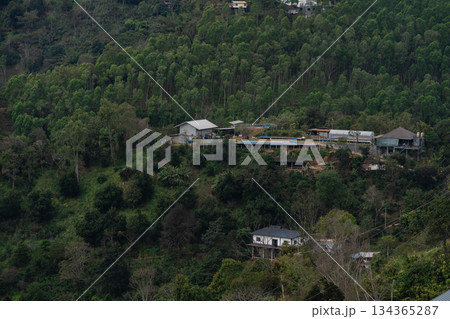 Tranquil hillside village surrounded by lush green forest featuring residential buildings and remote cabins in a peaceful natural setting Tranquil hillside village surrounded by lush green forest featuring residential buildings and remote cabins in a peaceful natural setting 134365287