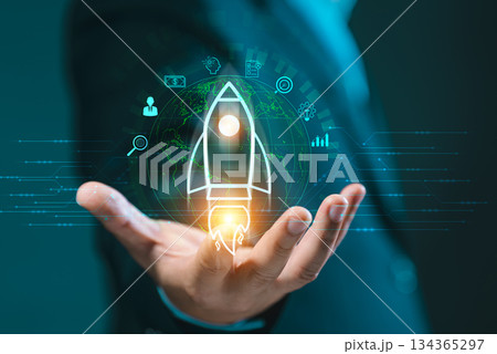 Hand presenting a glowing rocket icon over a global network, surrounded by business symbols. Signifies startup launch, innovation, future vision, and business acceleration. 134365297