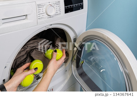 Woman Placing Tennis Balls into Clothes Dryer for Down Jacket Fluffing Process Indoors Woman Placing Tennis Balls into Clothes Dryer for Down Jacket Fluffing Process Indoors 134367641