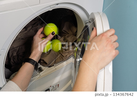 Fluffy Laundry Hack Woman Adding Tennis Balls to Dryer with Clothes for Extra Softness Fluffy Laundry Hack Woman Adding Tennis Balls to Dryer with Clothes for Extra Softness 134367642