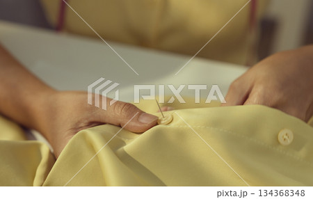 Asian woman threading the needle. Tailor working in her studio with focus in hands putting thread in sewing needle. 134368348
