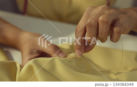 Asian woman threading the needle. Tailor working in her studio with focus in hands putting thread in sewing needle. Asian woman threading the needle. Tailor working in her studio with focus in hands putting thread in sewing needle. 134368349