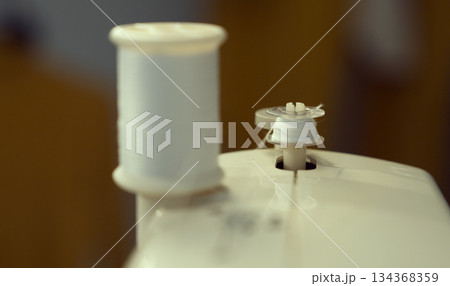 The bobbin is threaded with white thread on the sewing machine. The bobbin is threaded with white thread on the sewing machine. 134368359