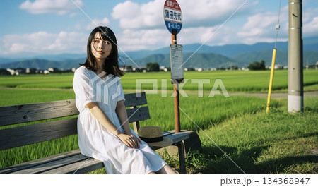 田舎のバス停のベンチで座る女性 134368947