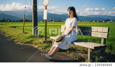 田舎のバス停のベンチで座る女性 134368948