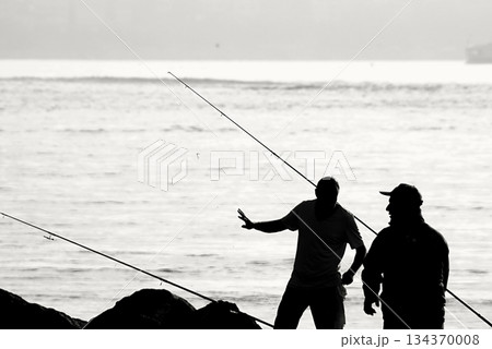 Silhouettes of Bosphorus fishermen in the early morning. A black-and-white, high-contrast image that captures the serene solitude of recreational fishing in Istanbul. 134370008