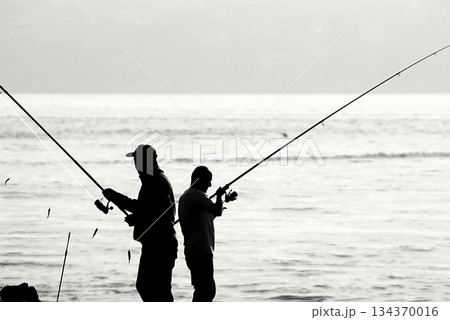 Silhouettes of Bosphorus fishermen in the early morning. A black-and-white, high-contrast image that captures the serene solitude of recreational fishing in Istanbul. 134370016