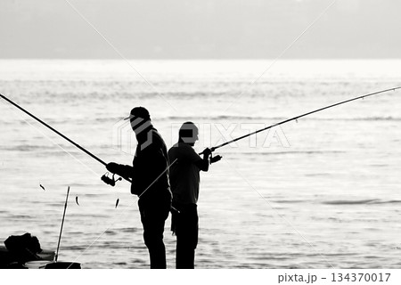Silhouettes of Bosphorus fishermen in the early morning. A black-and-white, high-contrast image that captures the serene solitude of recreational fishing in Istanbul. 134370017