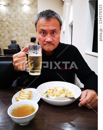 ビールを飲みながら炒飯、餃子を食べる男性 134370325