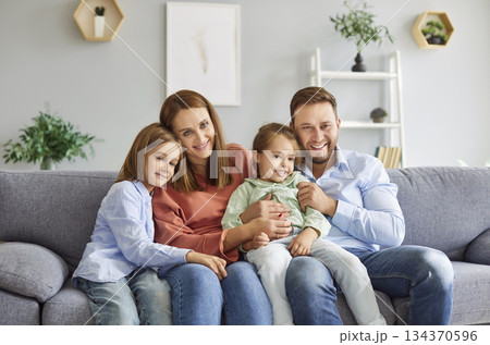Portrait of cheerful smiling young happy family of four with two kids sitting on sofa at home 134370596