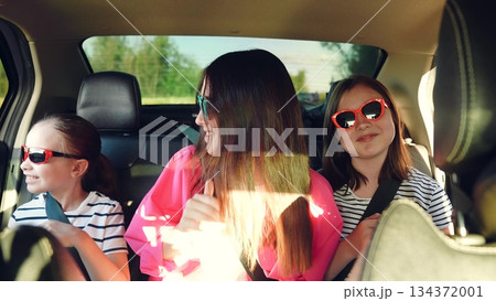 Happy family, girls riding car dancing having fun, child face smiling, mother child car trip, riding van summer party, happy family travel, mother with daughters, kids wearing sunglasses, children in 134372001