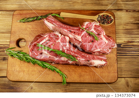 Raw fresh beef rib eye steaks on bone with spices and rosemary on wooden table. Top view Raw fresh beef rib eye steaks on bone with spices and rosemary on wooden table. Top view 134373074
