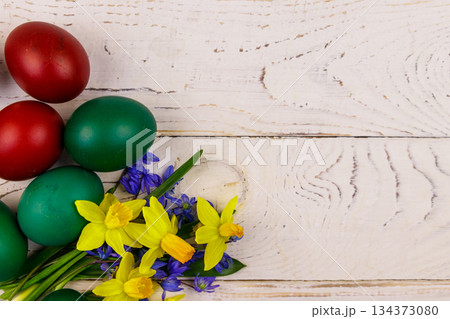 Painted Easter eggs and bouquet of yellow daffodils and blue scilla flowers on white wooden background. Easter composition. Top view, copy space 134373080