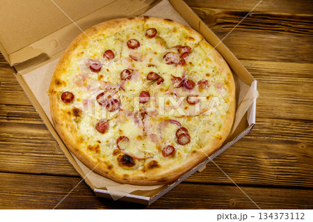 Delicious fresh pizza in cardboard box on a wooden table. Top view. Concept for home delivery of food, fast food, delivery of pizza 134373112