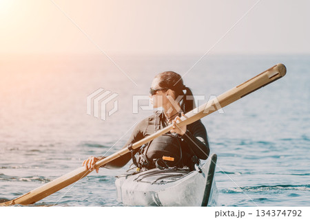 Kayaking Woman Paddle Ocean - A woman kayaks in the ocean at sunset, using a wooden paddle. 134374792