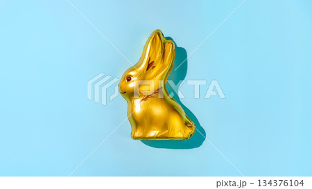 Golden chocolate rabbit in foil on a light blue background. 134376104