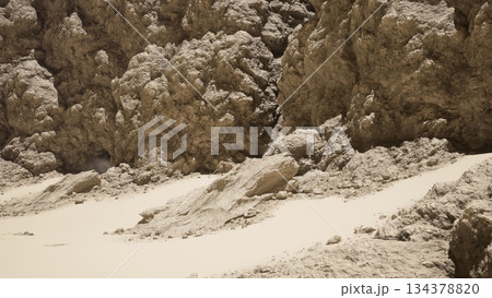 Adventurers navigate a harsh landscape filled with rough, textured rocks and smooth sandy areas. Bright sunlight casts shadows, creating a striking contrast in this remote location. 134378820