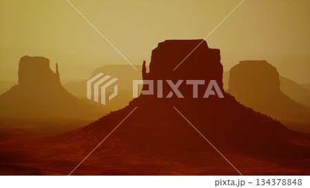 Silhouettes of unique rock formations stand tall against a stunning desert sunset. The warm golden light casts dramatic shadows, creating a serene atmosphere of natural beauty. 134378848