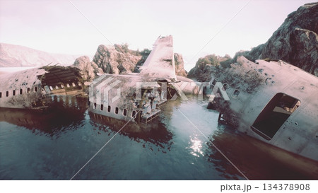 Amidst a serene landscape, the ruins of an airplane lie partially submerged in calm waters. The jagged rocks frame this haunting scene, hinting at a forgotten journey and lost stories. 134378908