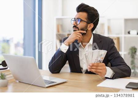 An Indian businessman contemplates his financial success while holding a stack of cash 134378981