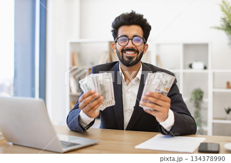 An Indian businessman smiles while holding a large amount of cash in his hands, celebrating financial success An Indian businessman smiles while holding a large amount of cash in his hands, celebrating financial success 134378990