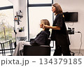 Professional female Hairdresser styling hair for woman client in black clothes, side view inside modern beauty salon with natural light and contemporary interior 134379185