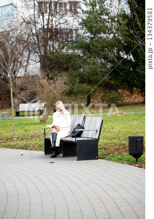 Woman enjoying a peaceful moment reading on a bench in a tranquil park surrounded by nature's beauty during a serene afternoon 134379581