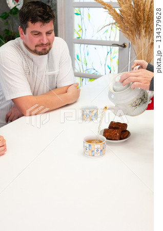 Enjoying a warm afternoon tea surrounded by friends with freshly baked treats and cozy conversations in a delightful kitchen setting 134379628