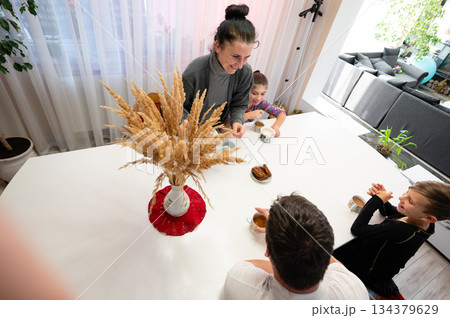 Family gathering at a cozy kitchen table with warm beverages and sweet pastries, capturing joyful moments and connections in a bright and inviting home space Family gathering at a cozy kitchen table with warm beverages and sweet pastries, capturing joyful moments and connections in a bright and inviting home space 134379629