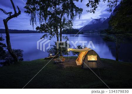 Night camping adventure with a cozy tent lit under the starry sky in a summer forest 134379830